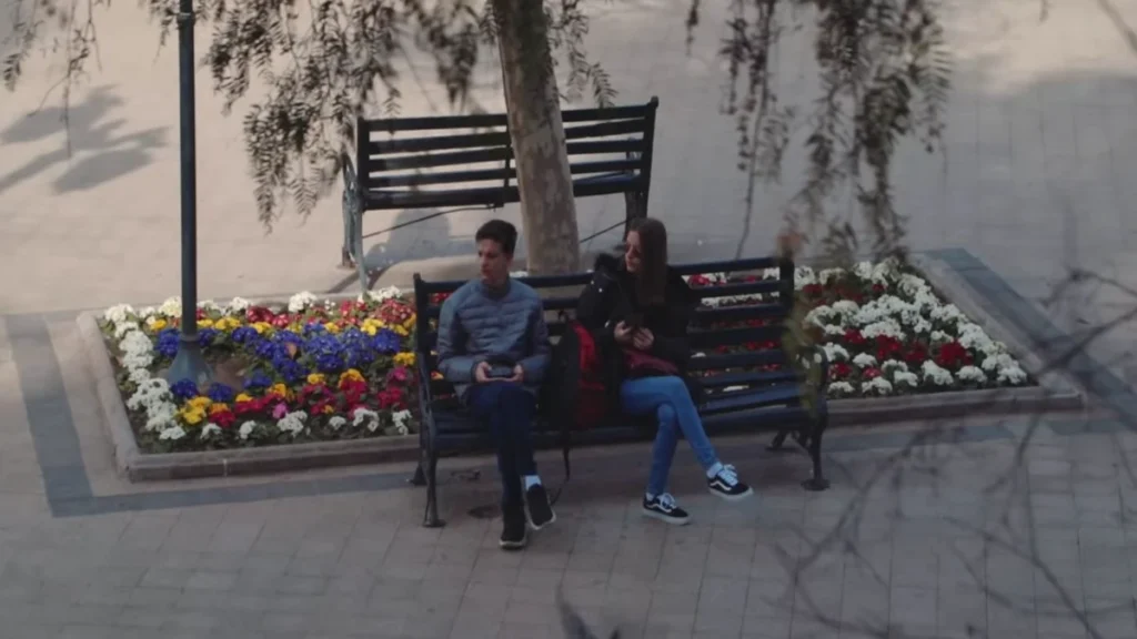 Casal sentado em banco de praça rodeado por flores coloridas em Santiago.