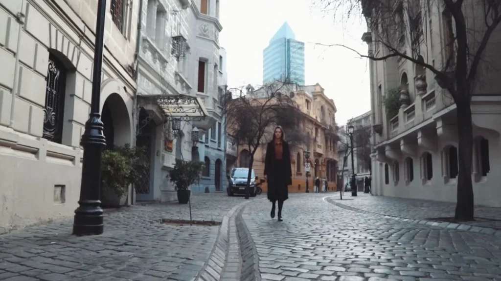 Mulher caminhando por uma rua de paralelepípedos com edifícios históricos ao fundo em Santiago.
