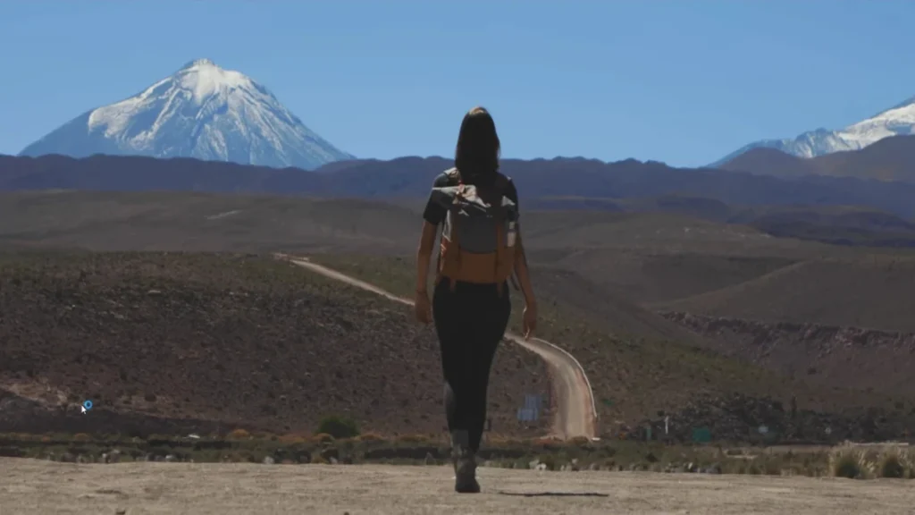Uma mulher caminhando no Deserto de Atacama com uma grande montanha ao fundo.
