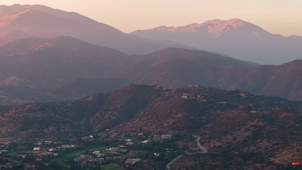 Vista aérea de bairros residenciais de Santiago com montanhas dos Andes ao fundo durante o pôr do sol