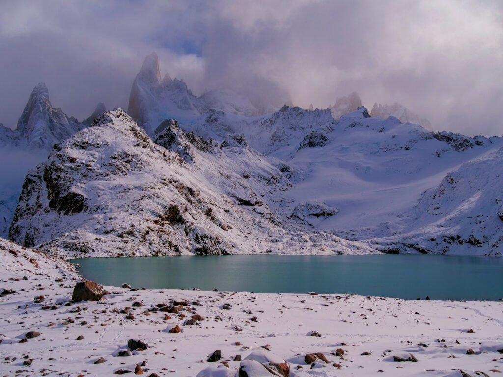 uma cadeia de montanhas coberta de neve com um lago em primeiro plano