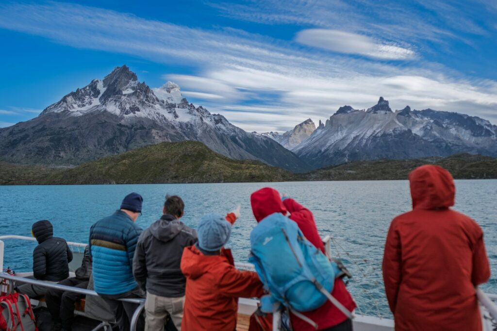 Pessoas observam montanhas de um barco na água.