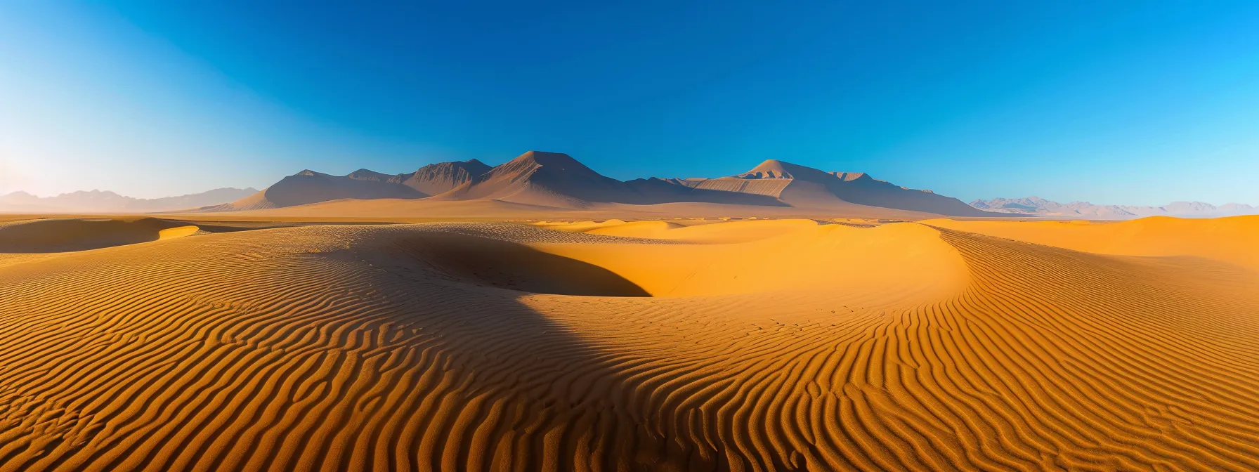 uma vista panorâmica deslumbrante do deserto de atacama ao amanhecer, com suas dunas douradas e formações rochosas contrastando com o céu azul profundo, simbolizando a aventura e a beleza natural da região.