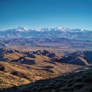 uma paisagem impressionante do chile, capturando as montanhas nevadas dos andes ao fundo, sob um céu azul claro que se estende sobre os vales centrais, enquanto colinas desérticas secas predominam em primeiro plano, ilustrando as drásticas variações climáticas do país.
