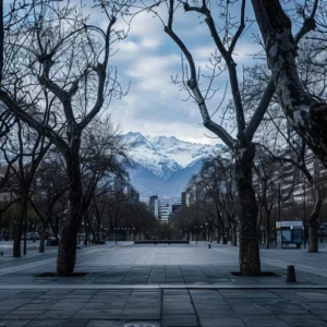 uma cena urbana de santiago em junho, com um céu nublado e os andes cobertos de neve ao fundo, apresentando uma praça tranquila com árvores sem folhas, refletindo a calma de um dia frio de inverno.
