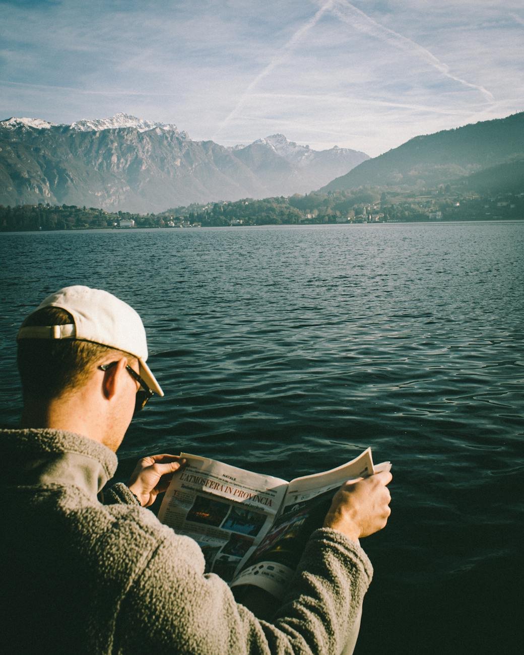 homem lendo jornal perto do lago e das montanhas