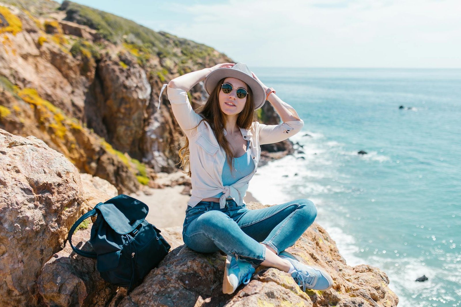 mulher de camisa branca e calça jeans azul sentada em uma rocha perto do mar