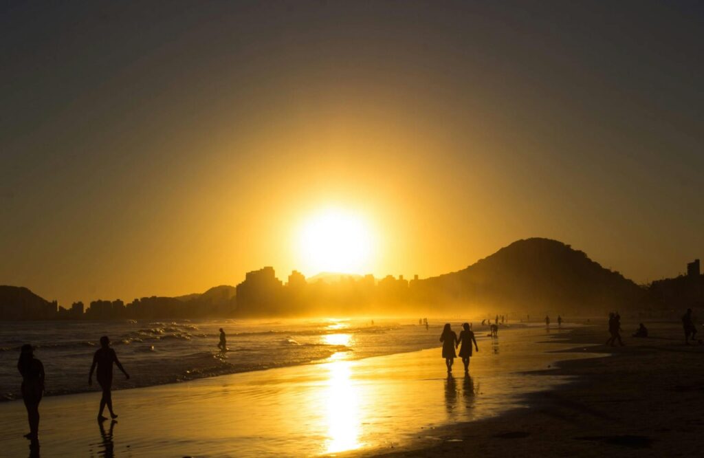 Silhuetas ao pôr-do-sol na praia do Guarujá, Brasil, com um horizonte dourado.