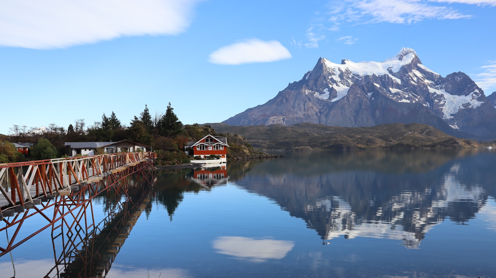O lago reflete montanhas e cabanas sob um céu azul.