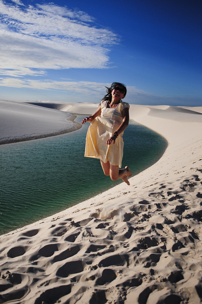  Turista pulando de alegria nas dunas de areia branca ao lado de uma lagoa azul nos Lençóis Maranhenses.