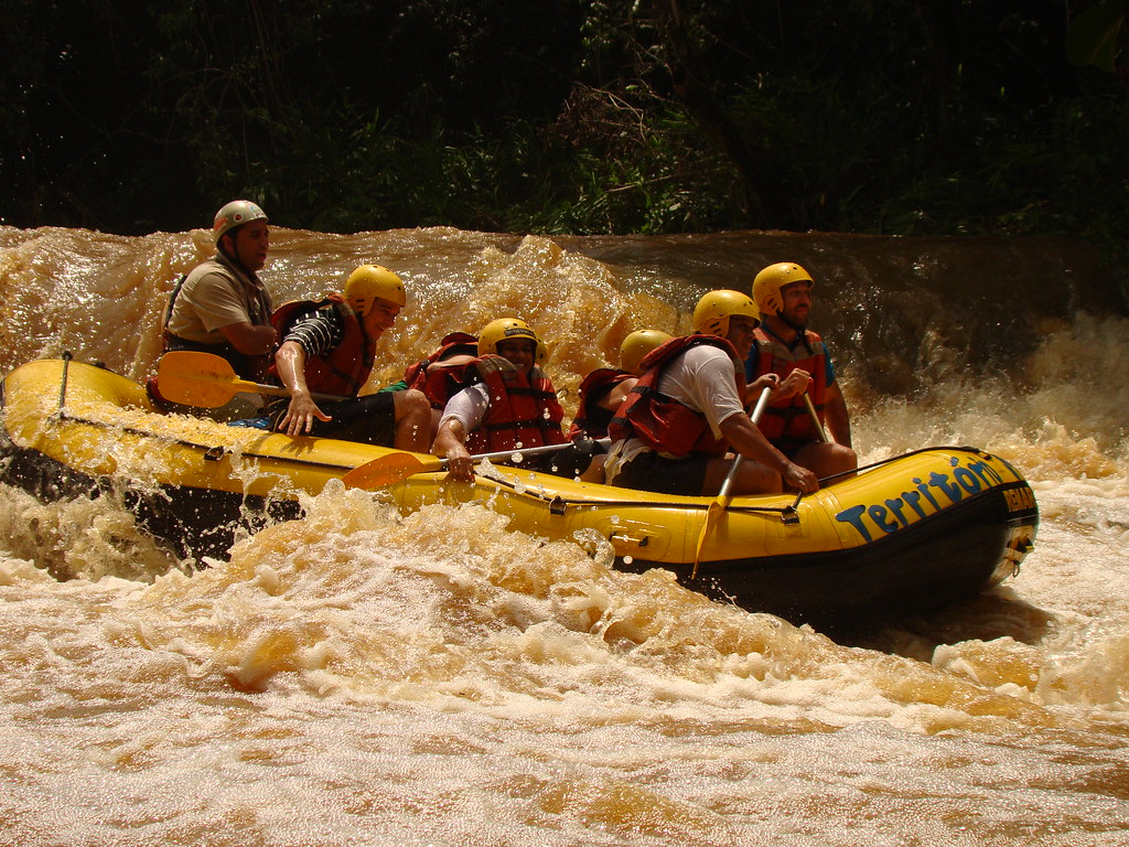 Grupo de pessoas praticando rafting em bote amarelo nas corredeiras agitadas de um rio em Brotas.