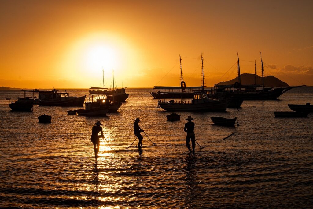 Pescadores puxando rede no mar durante o pôr do sol em praia brasileira, representando a cultura local.