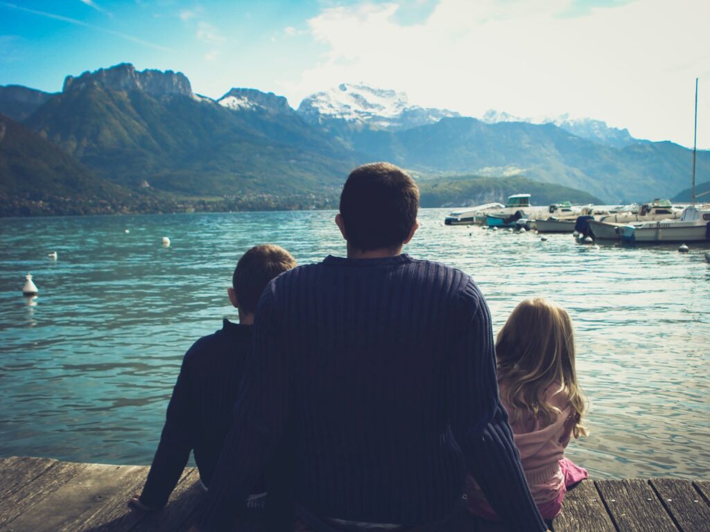 Família sentada em um píer de madeira observando um lago e montanhas, planejando dicas de viagem em família.