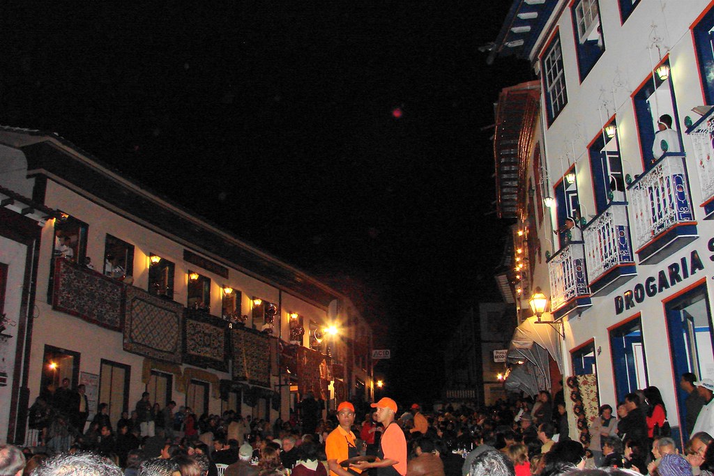 Músicos tocando instrumentos nas sacadas iluminadas de casarões coloniais à noite, enquanto uma multidão assiste sentada em mesas na rua de pedra durante a Vesperata em Diamantina.