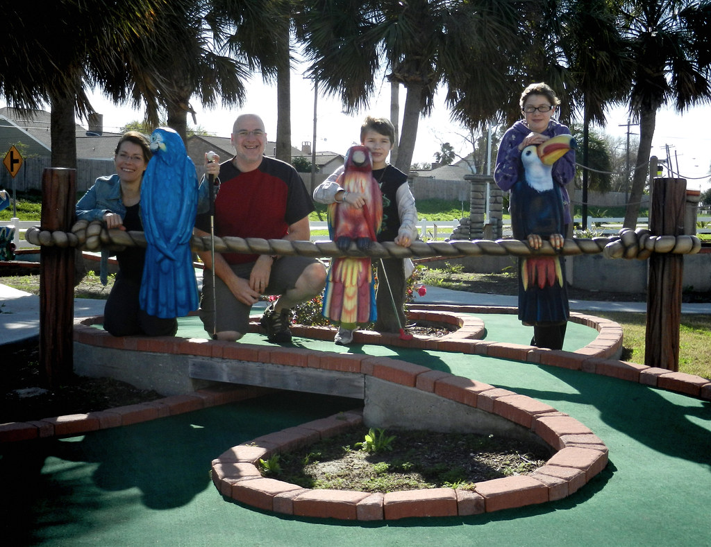 Família com dois filhos posando felizes em um campo de minigolfe temático durante as férias.