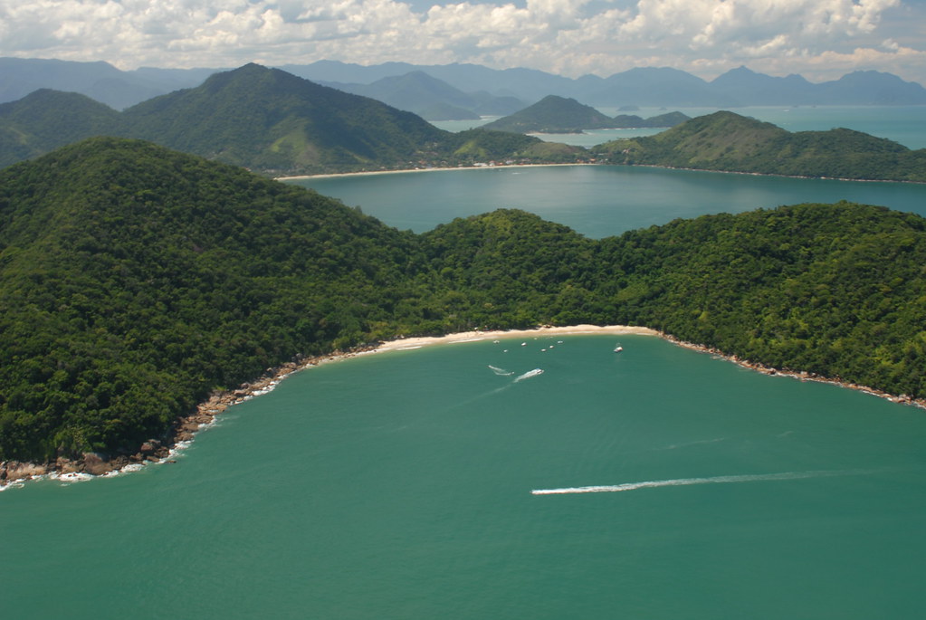 Vista aérea de uma baía com águas verdes cercada por Mata Atlântica preservada, opção para roteiros de férias familiares curtos.