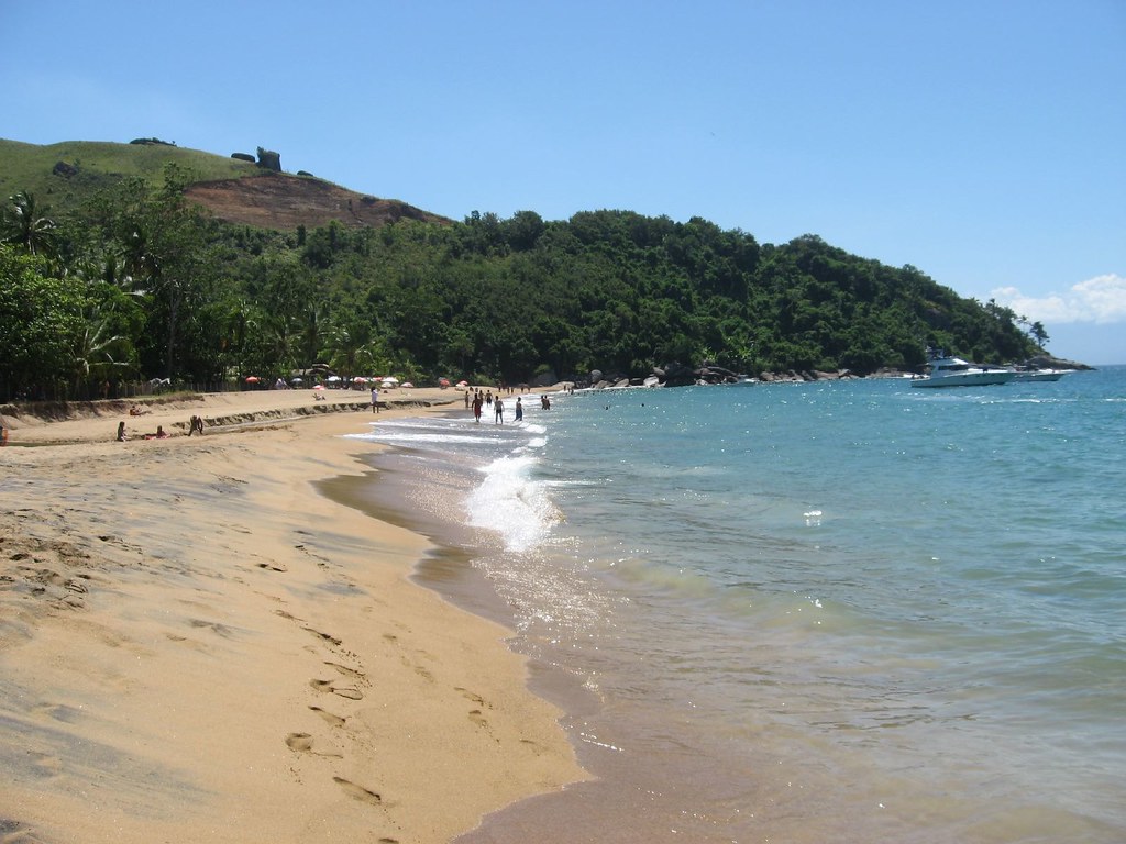 Praia de areia dourada e mar calmo cercada por mata atlântica em Ilhabela, destino de turismo ecológico no Brasil, em São Paulo.