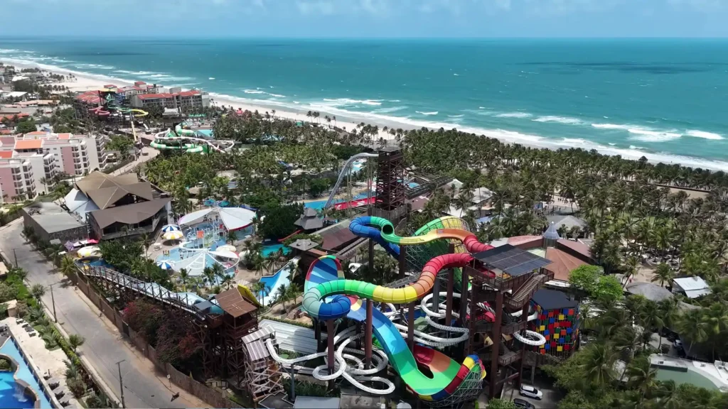Vista aérea panorâmica do parque aquático Beach Park em Fortaleza, mostrando toboáguas coloridos, piscinas e o mar ao fundo.