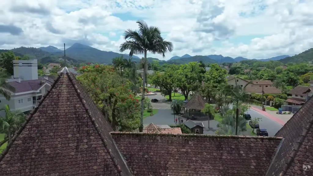 Vista aérea aproximada do centro de Pomerode, focando nos telhados de cerâmica, no coreto tradicional da praça e na vegetação urbana.