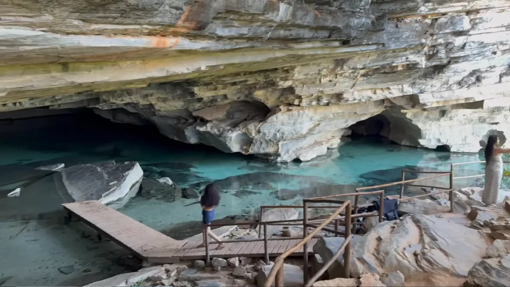 Mulher em plataforma de madeira observando lagoa azul dentro de uma caverna.