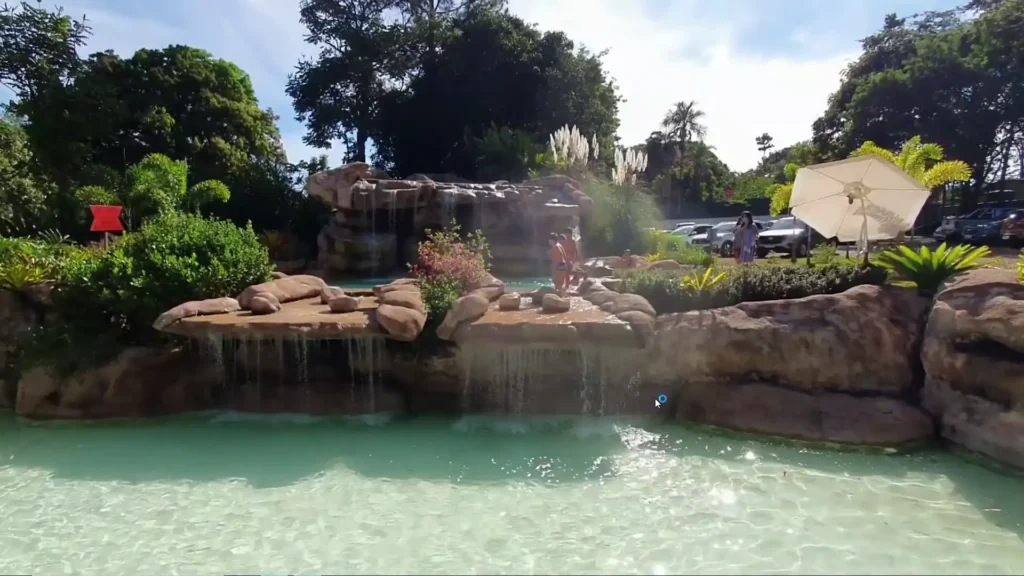 Crianças brincando em cachoeiras artificiais e piscinas naturais em dia de sol.