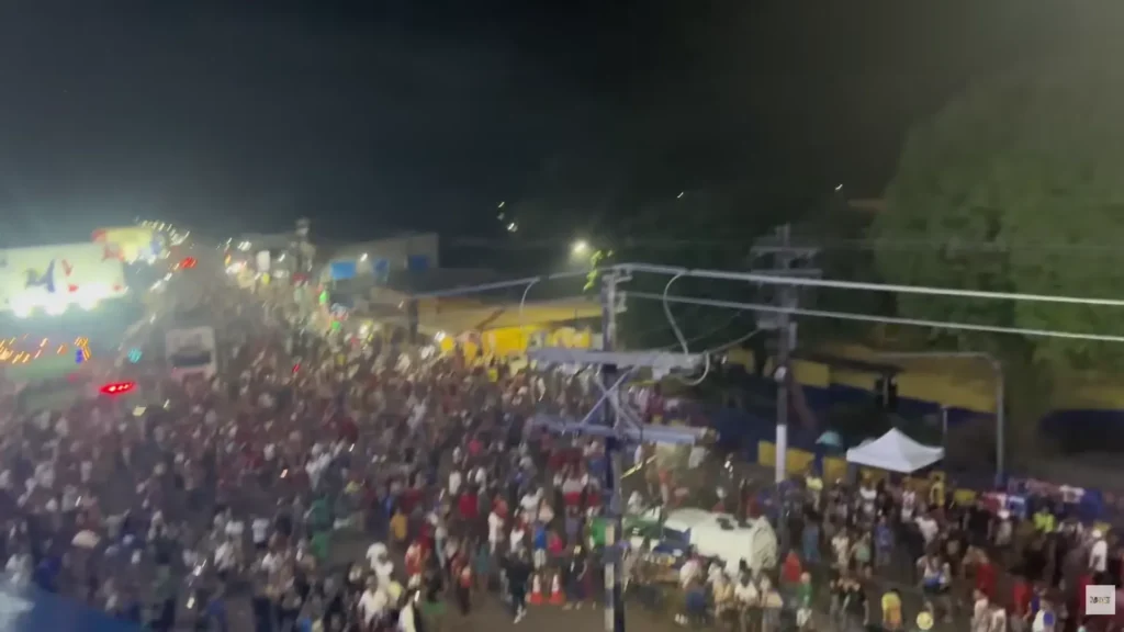 Multidão reunida nas ruas à noite celebrando festividades populares típicas da cultura local do Brasil.