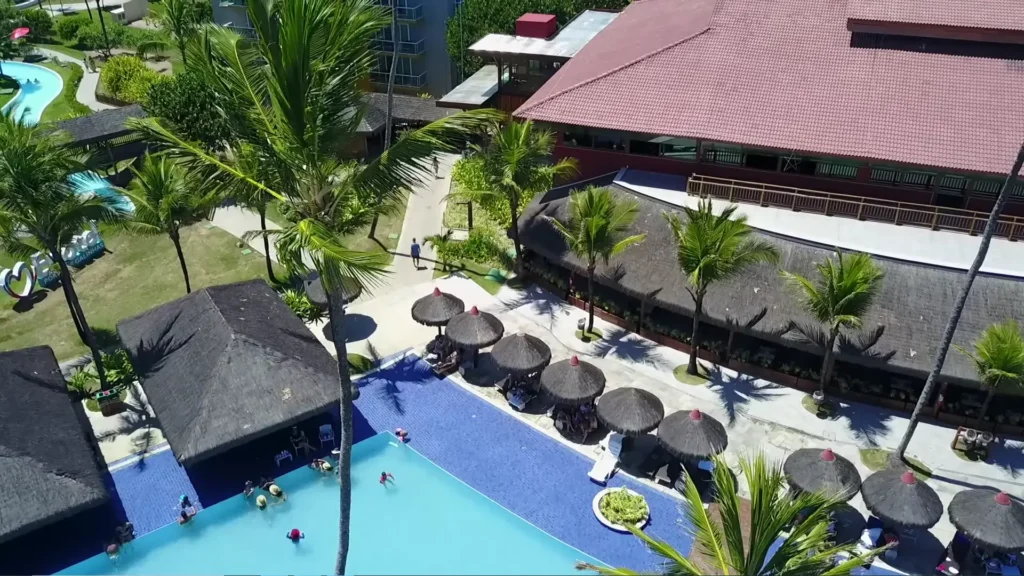 Área de lazer do resort com piscina, bar molhado e quiosques de palha.