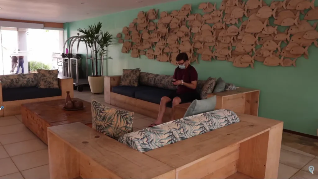 Lounge de entrada do hotel com decoração de peixes na parede e sofás de madeira.