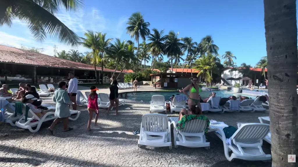 Hóspedes aproveitando a piscina do Pratagy Beach Resort com espreguiçadeiras e coqueiros ao fundo.