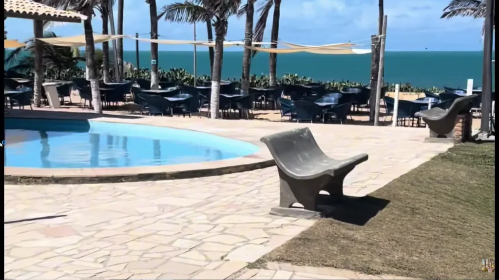 Área da piscina com banco de design moderno, deck de pedra e vista para o mar azul e coqueiros no Coliseum Beach Resort.