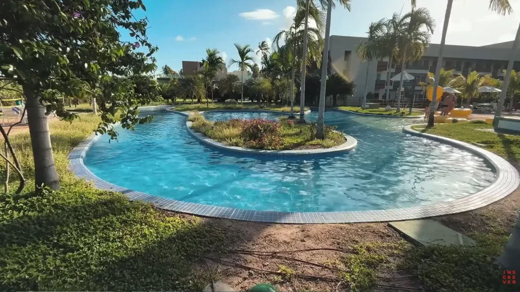 Piscina com formato orgânico cercada por jardins no Japaratinga Lounge Resort.