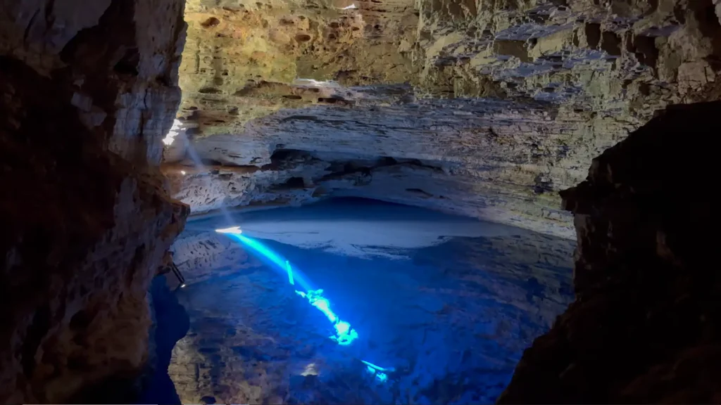 Raio de sol iluminando a água azul turquesa dentro de uma caverna escura.