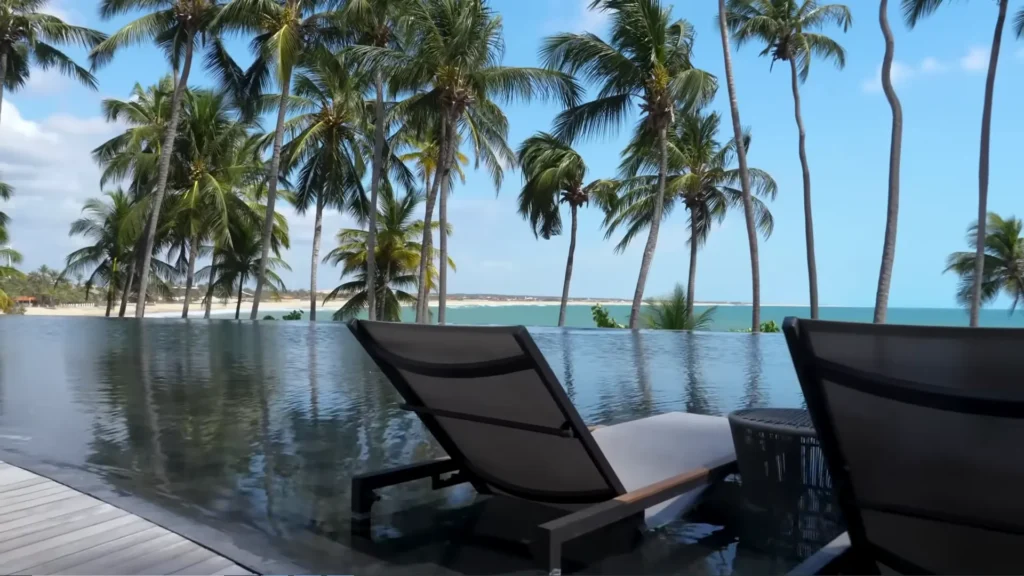 Espreguiçadeira dentro da piscina de borda infinita do Carmel Taíba Resort com vista para o mar e coqueiros.
