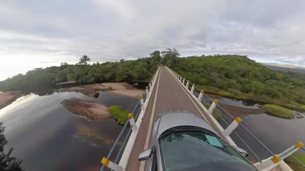 Vista de dentro de um carro atravessando uma ponte sobre um rio cercado por mata.