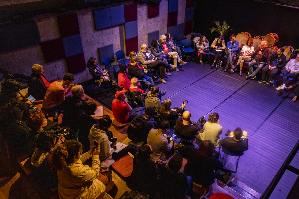 Roda de conversa e debate sobre a cultura local Brasil em teatro com plateia e convidados sentados em círculo.