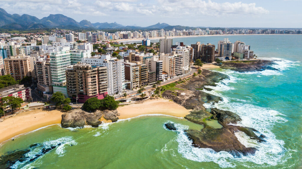 vista aérea da orla de Guarapari com mar calmo e prédios, um dos principais lugares para passear com crianças no litoral do Espírito Santo.