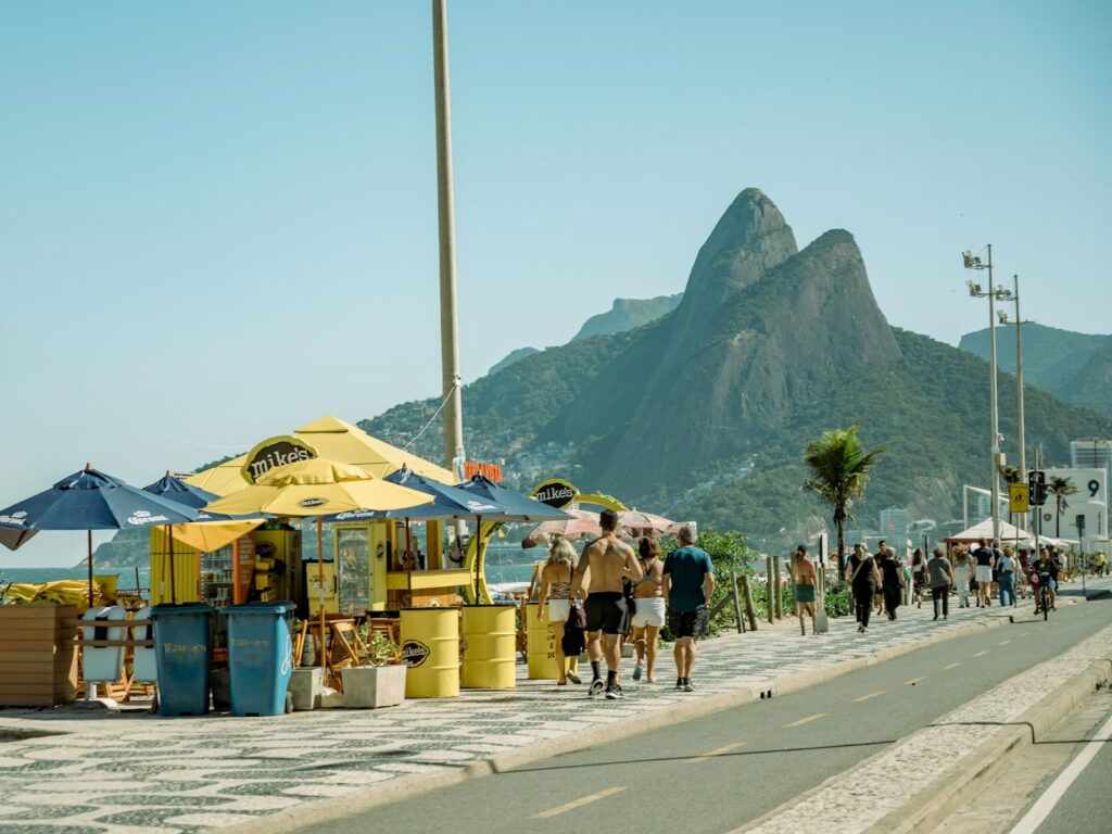 pessoas caminhando no calçadão da orla do Rio com o Morro Dois Irmãos ao fundo, clássico entre os lugares para passear com crianças na cidade maravilhosa.