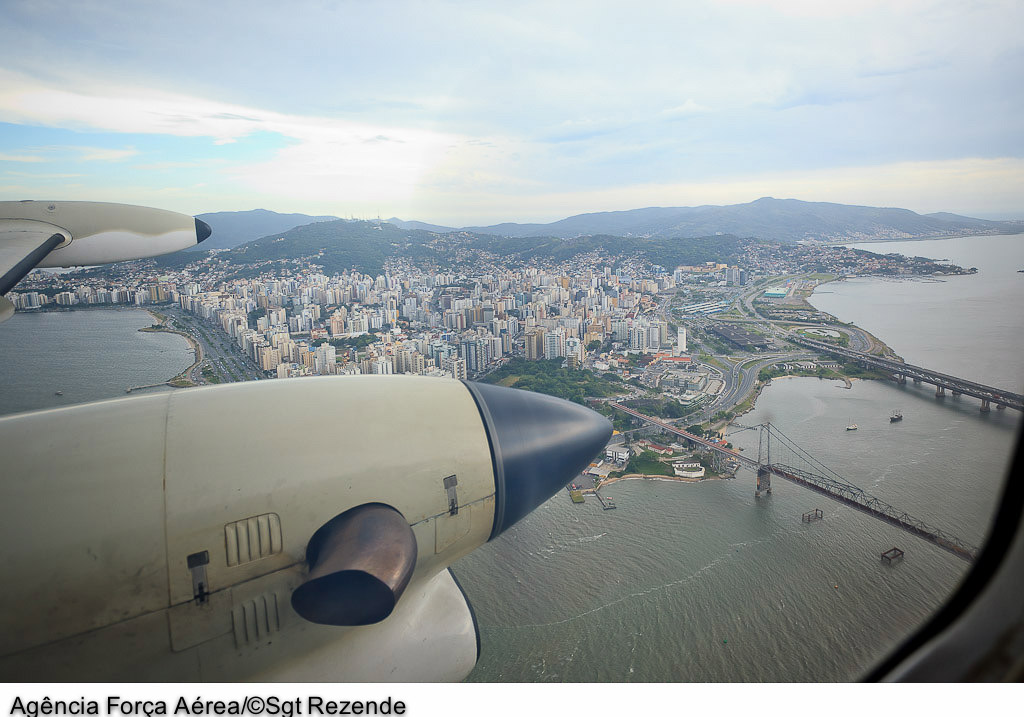Vista da janela de um avião chegando em Florianópolis, mostrando a Ponte Hercílio Luz e a baía norte da ilha.