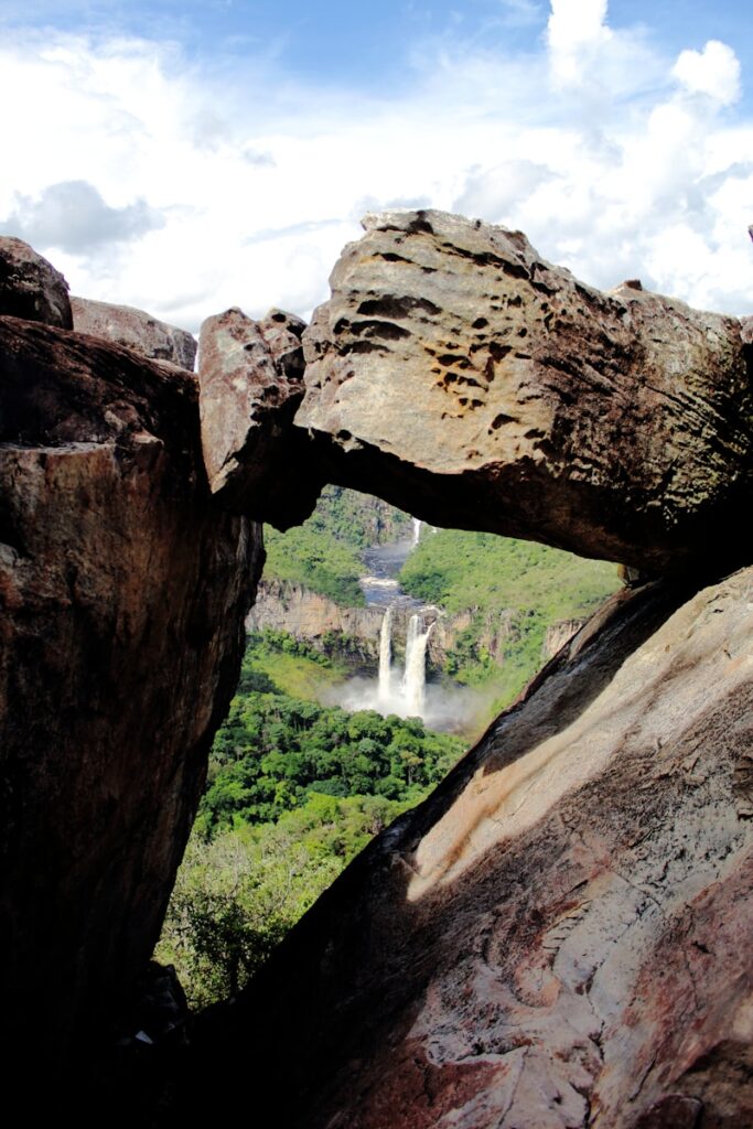 Arch rock frames distant waterfalls and lush green forest