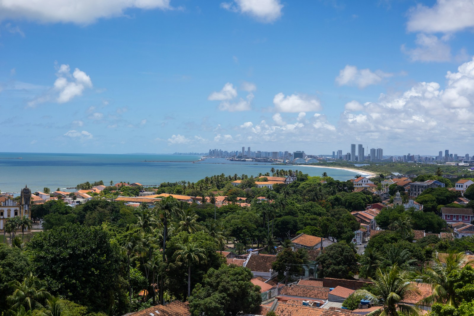 Vista dos prédios históricos coloridos do Recife Antigo à beira do rio, com barcos ancorados em primeiro plano.