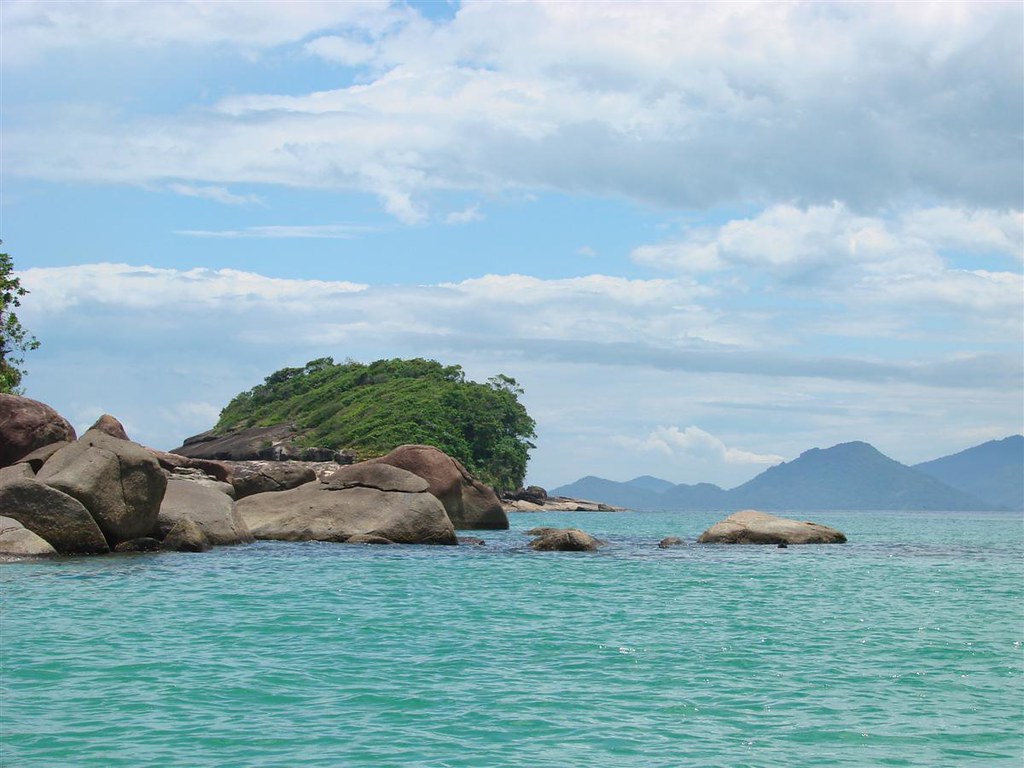 Vista do mar calmo de águas esverdeadas e pedras na orla de Ubatuba, litoral de São Paulo.