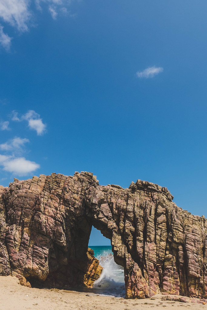 Formação rochosa da Pedra Furada na praia de Jericoacoara, Ceará, com ondas quebrando ao fundo.