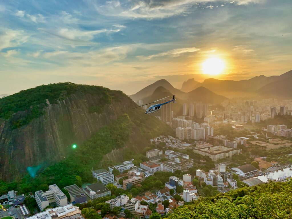 Helicóptero sobrevoando o Rio de Janeiro ao pôr do sol com o Corcovado ao fundo.