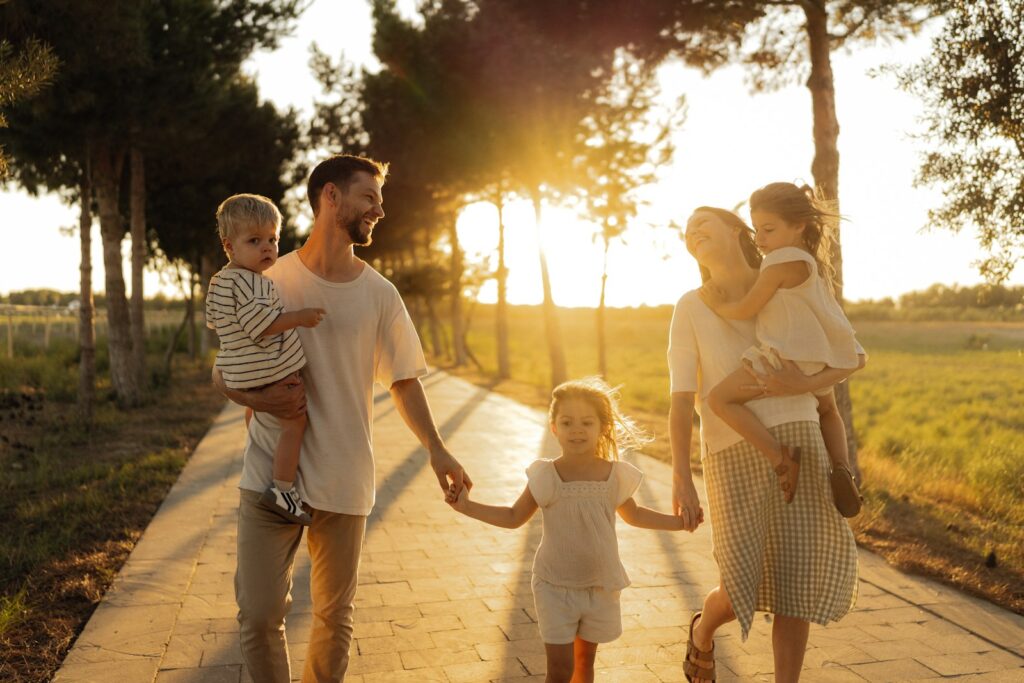 Família com três filhos pequenos caminhando em um parque ao pôr do sol durante as férias.
