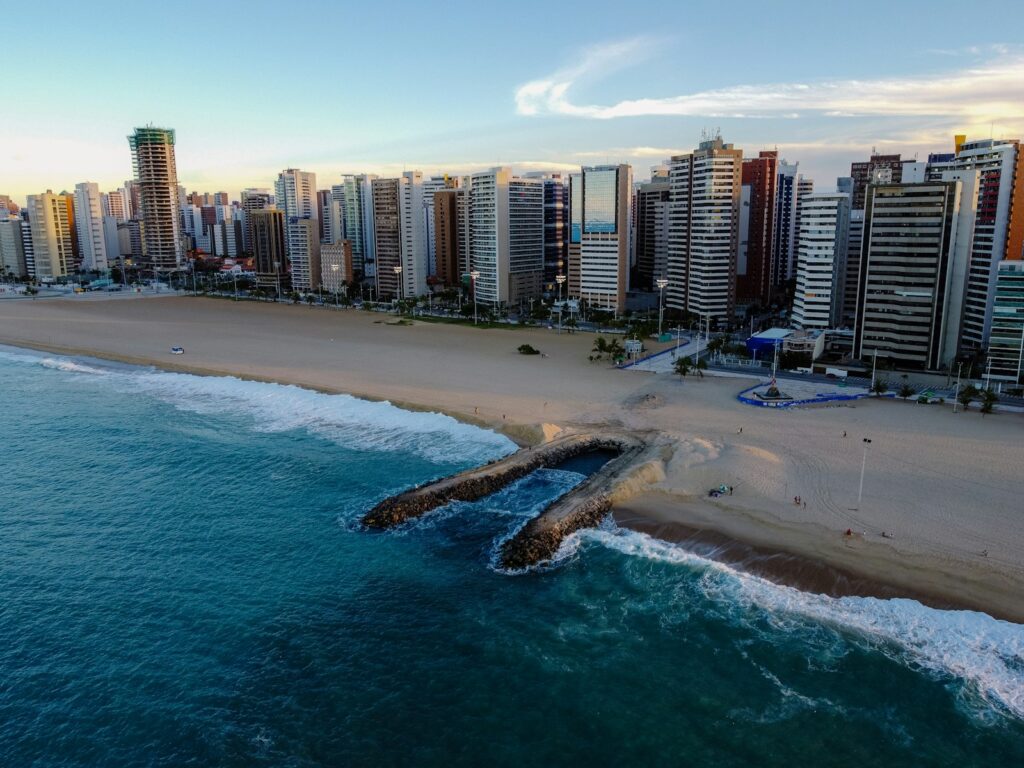 Vista aérea panorâmica da orla da praia de Fortaleza com prédios altos ao fundo e mar azul.