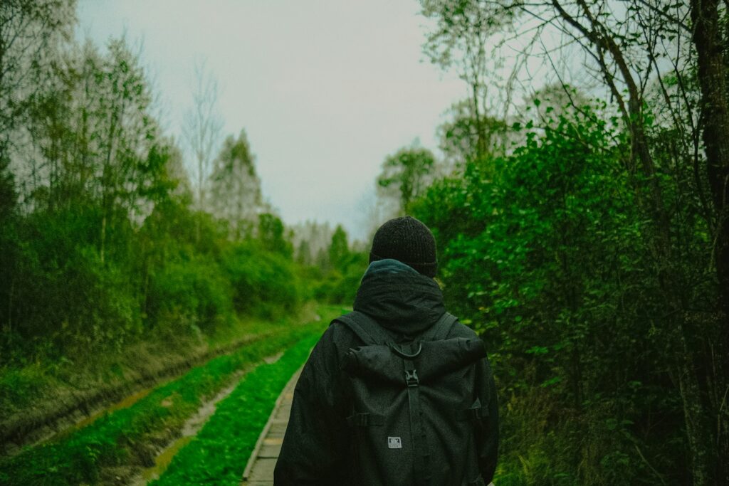 Pessoa de costas com mochila caminhando em uma trilha verde na floresta.