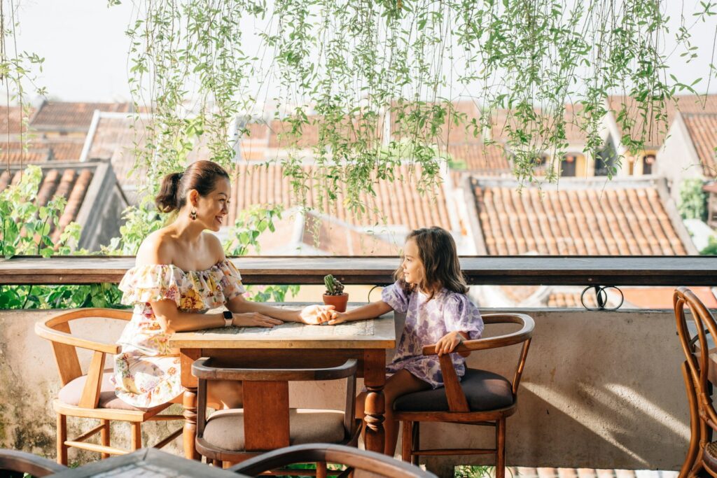 Mãe e filha pequena sentadas sorrindo em uma mesa de restaurante em hotel com vista para cidade.