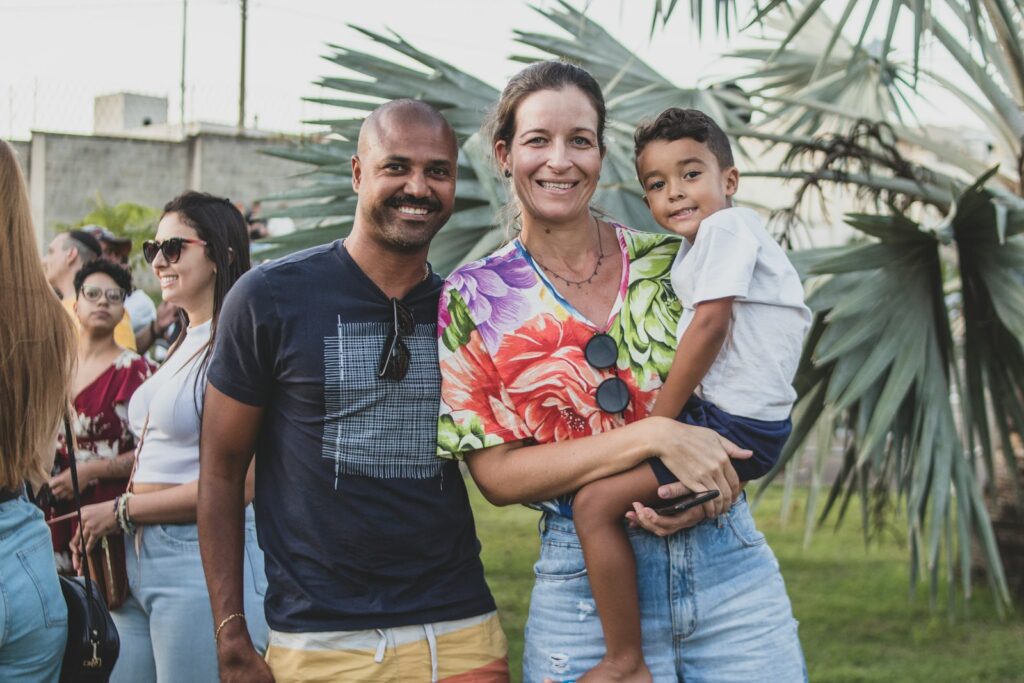 Pai, mãe e filho sorrindo abraçados em um parque durante um dos roteiros de férias familiares no Brasil.