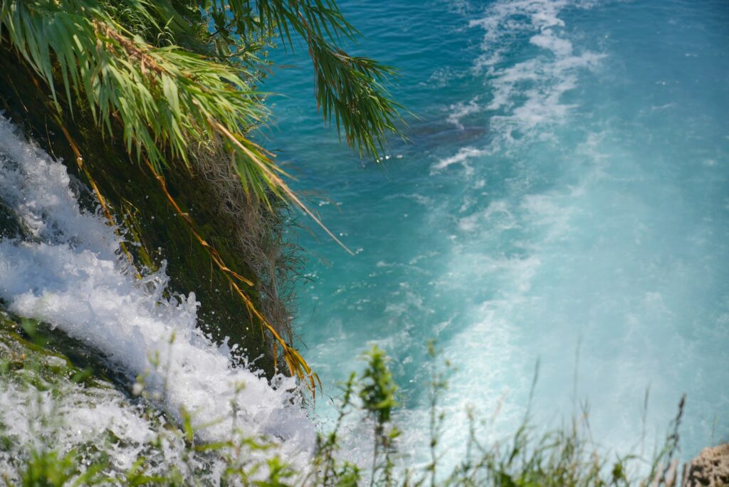 Close-up de uma cachoeira com água azul cristalina caindo sobre pedras e vegetação verde.
