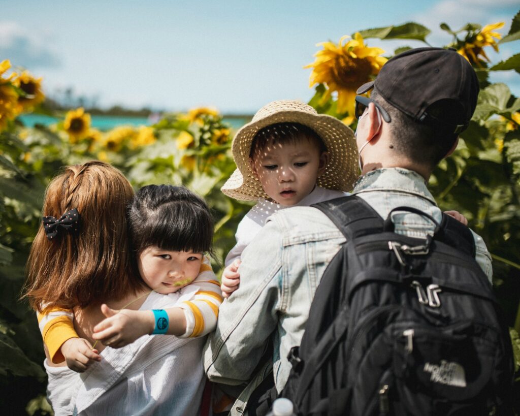 Pais carregando filhos pequenos em passeio na natureza, ilustrando cuidados em roteiros de férias familiares.